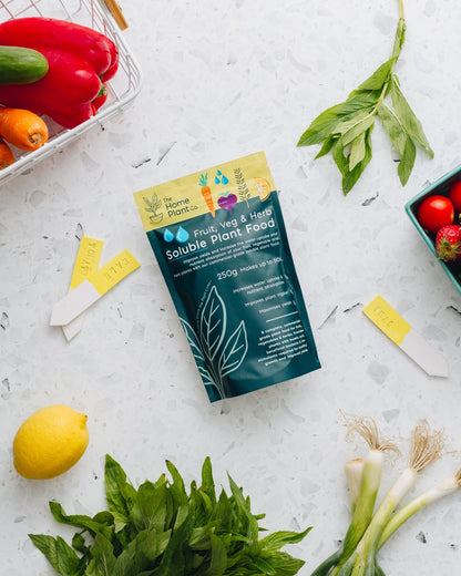 Fruit, Veg & Herb Soluble Fertiliser lying on a bench beside fresh fruit and vegetables